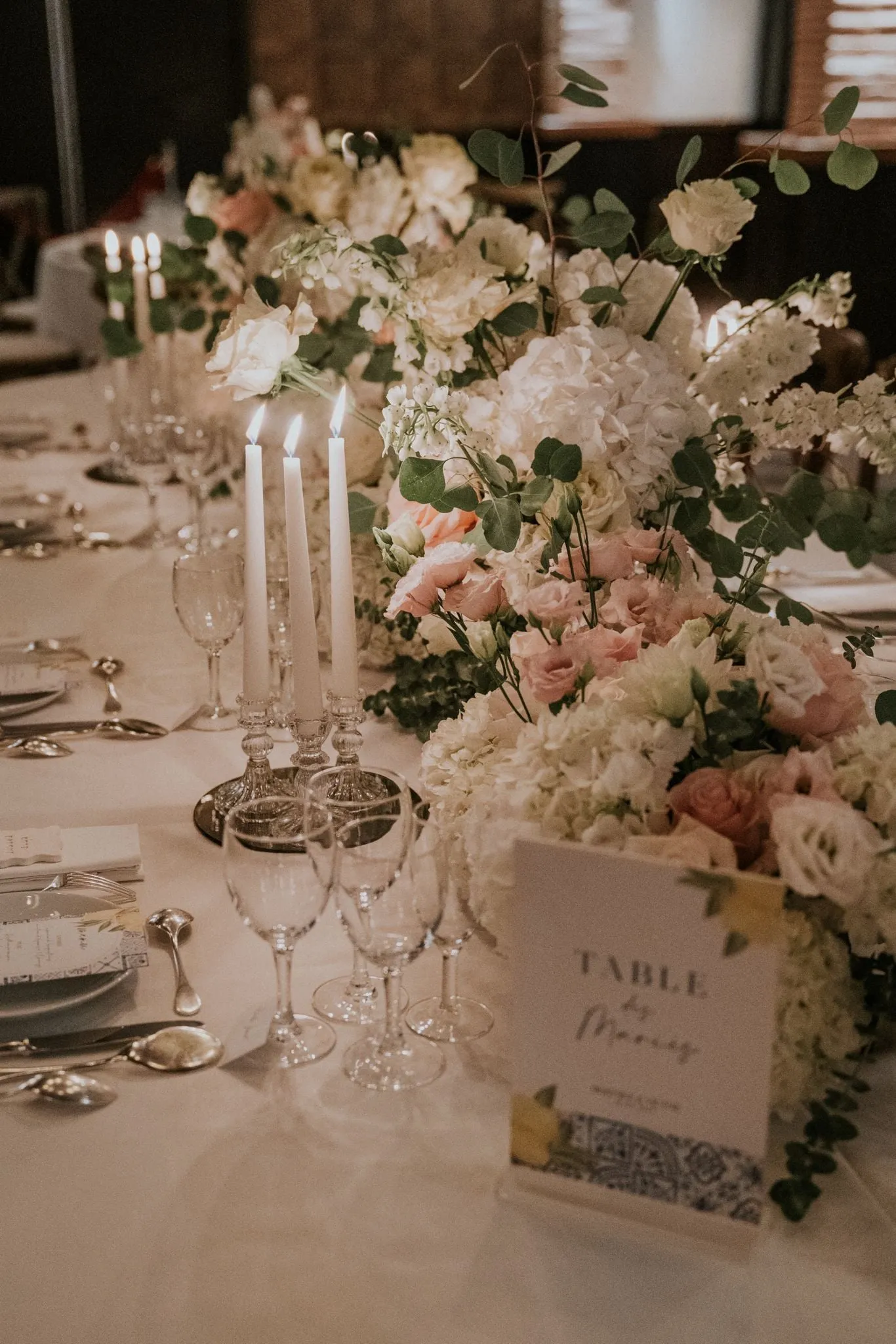 Table de mariage fleurie de roses pâles, bougies et verres en cristal