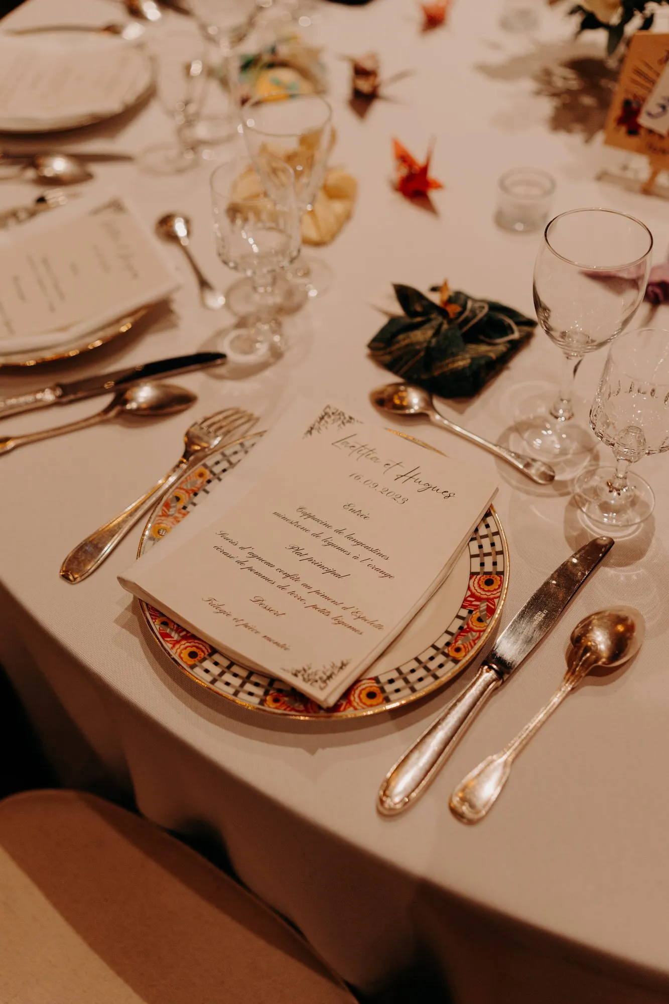Détail d'une table de mariage : menu, assiette dorée et verres en cristal